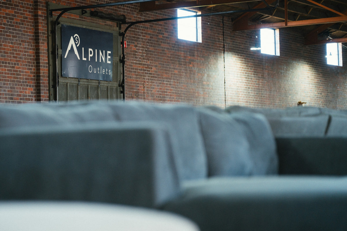 The Alpine Outlets sign on the brick wall of the Denver warehouse, behind a row of sectional sofas